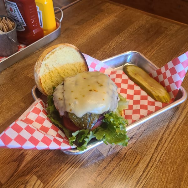 A Longhorn Outpost & Barbeque Company burger with melted cheese, lettuce, tomato, and a pickle spear.