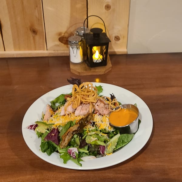 A Longhorn Outpost & Barbeque Company salad with sliced meat, crispy onions, cheese, and dressing.
