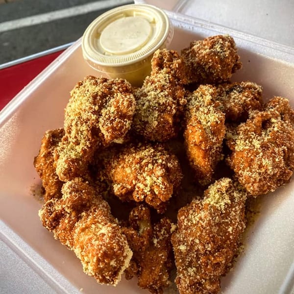 Crispy, breaded chicken wings with parmesan cheese and a side of dipping sauce in a white container.